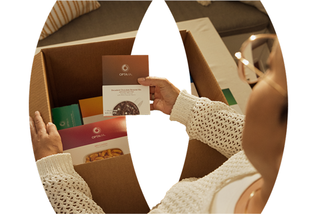 Woman unboxing a cardboard container filled with Optavia Products and a guide book